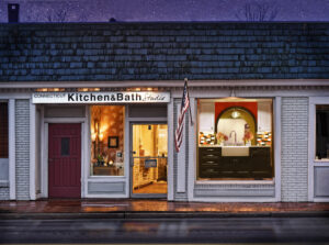 Storefront of Connecticut Kitchen & Bath Studios at night, lights on inside, American flag displayed outside.