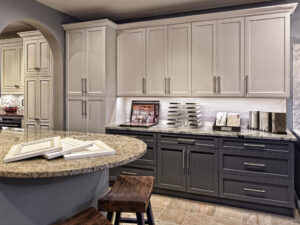 Modern kitchen with gray and white cabinetry, granite countertops, and wooden stools at a curved island.