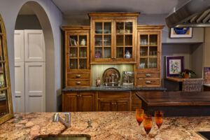 Wooden kitchen cabinets with glass doors, a marble countertop, and three orange glasses placed on the island in front.