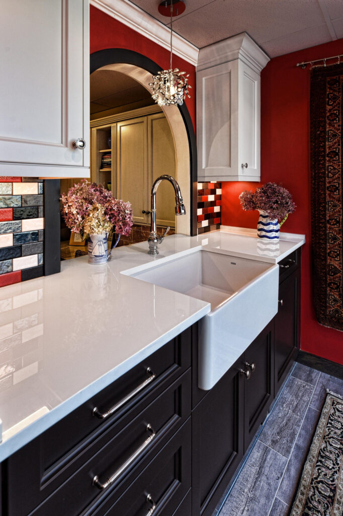 Modern kitchen with white countertops, farmhouse sink, red walls, mosaic backsplash, and floral vases on the counter.